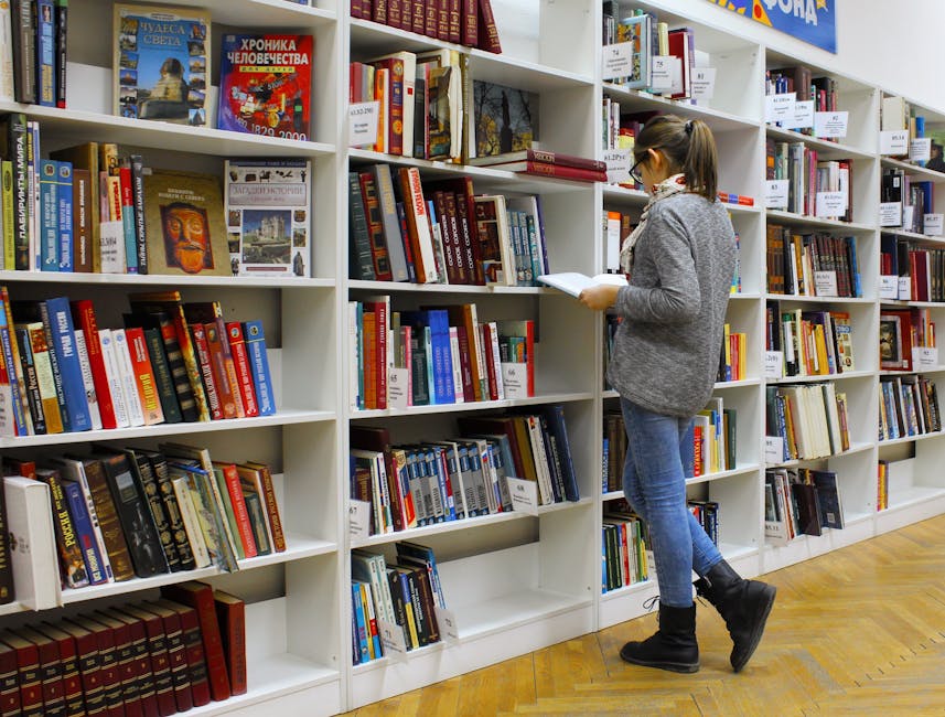 A young woman stands reading a book in a well-stocked library